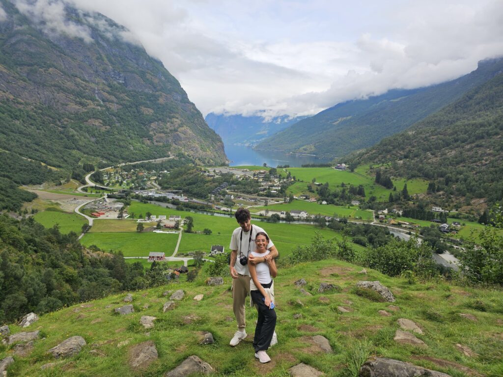 Dos personas en una colina con vistas a un valle verde y un fiordo en Noruega